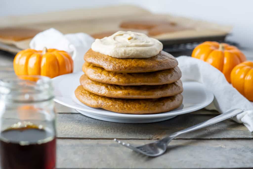 Side view of a stack of four finished fluffy paleo pancakes with a swirl of vegan pumpkin spice whipped cream on top!