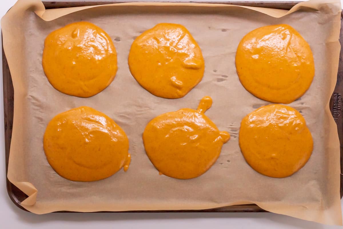 Six uncooked pancake rounds on a large baking sheet covered in parchment paper.