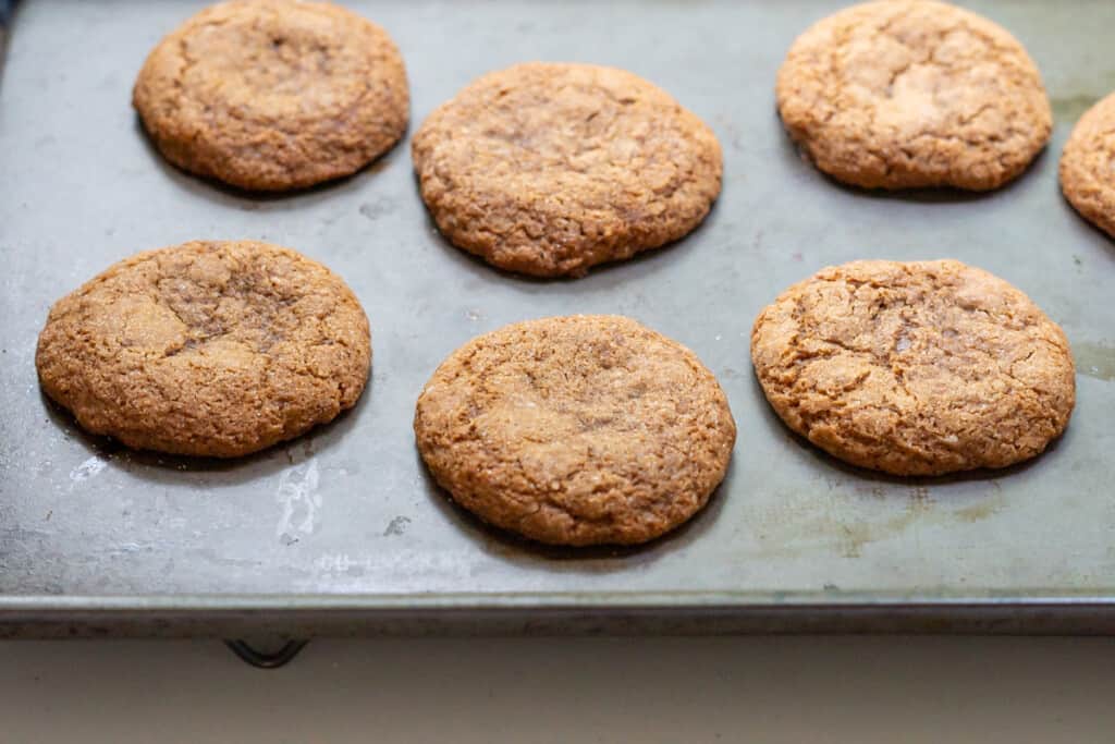Side view of a baking sheet with freshly baked paleo ginger molasses cookies with browned edges and a slightly crackled top.
