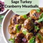 Side view of Turkey Cranberry Meatballs with smooth buttery gravy and garnished with dried cranberries and chopped parsley in a serving dish on a festively decorated table.