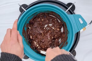 Overhead view of a pot of melted chocolate with pieces of chopped almonds and dried cranberries.