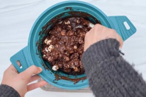 Overhead view of a hand with a spatula stirring mini marshmallows into a chocolate mixture.