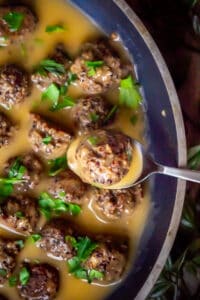 Overhead view of vegan swedish meatballs in a skillet with a close up of one on a spoon to show the outer texture with quinoa and bits of mushrooms.