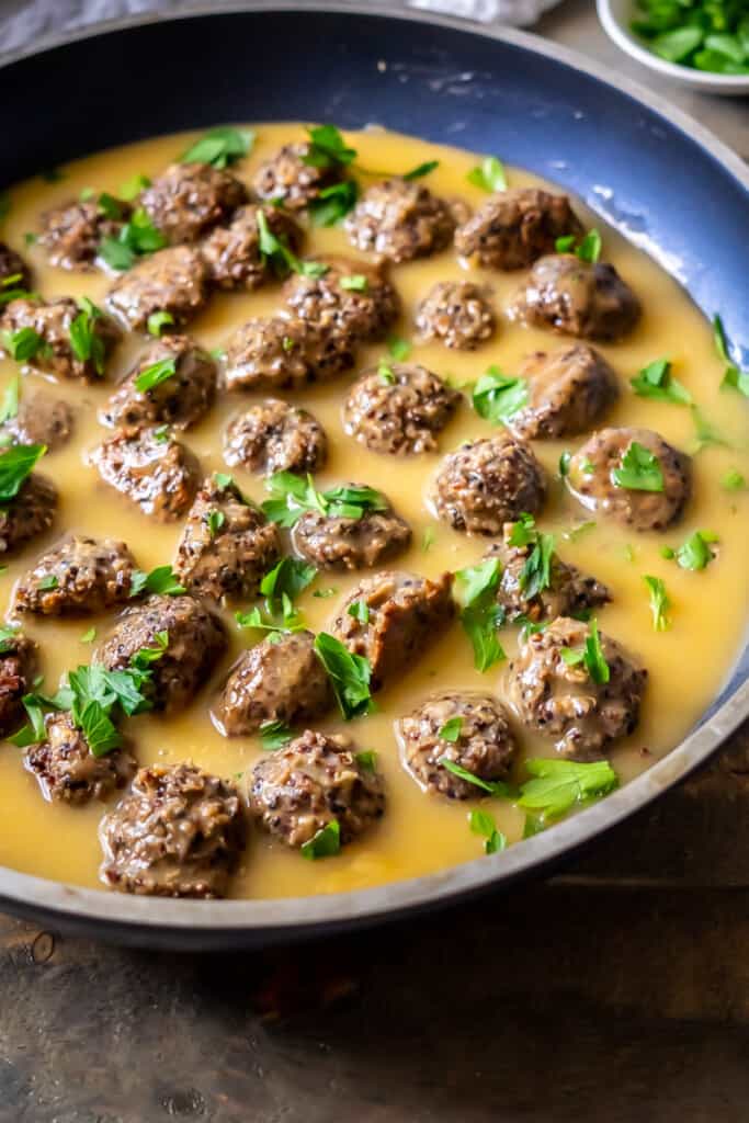 Side view of a skillet filled with vegan swedish meatballs in a buttery vegan gravy.
