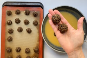 Overhead view of the cooked vegan meatballs on a baking sheet with a silicone liner and two in a hand for a close up of the cohesive texture.