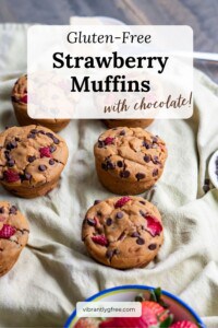 Six gluten free strawberry muffins with chocolate chips served with a side of dairy-free butter and a side of strawberries.
