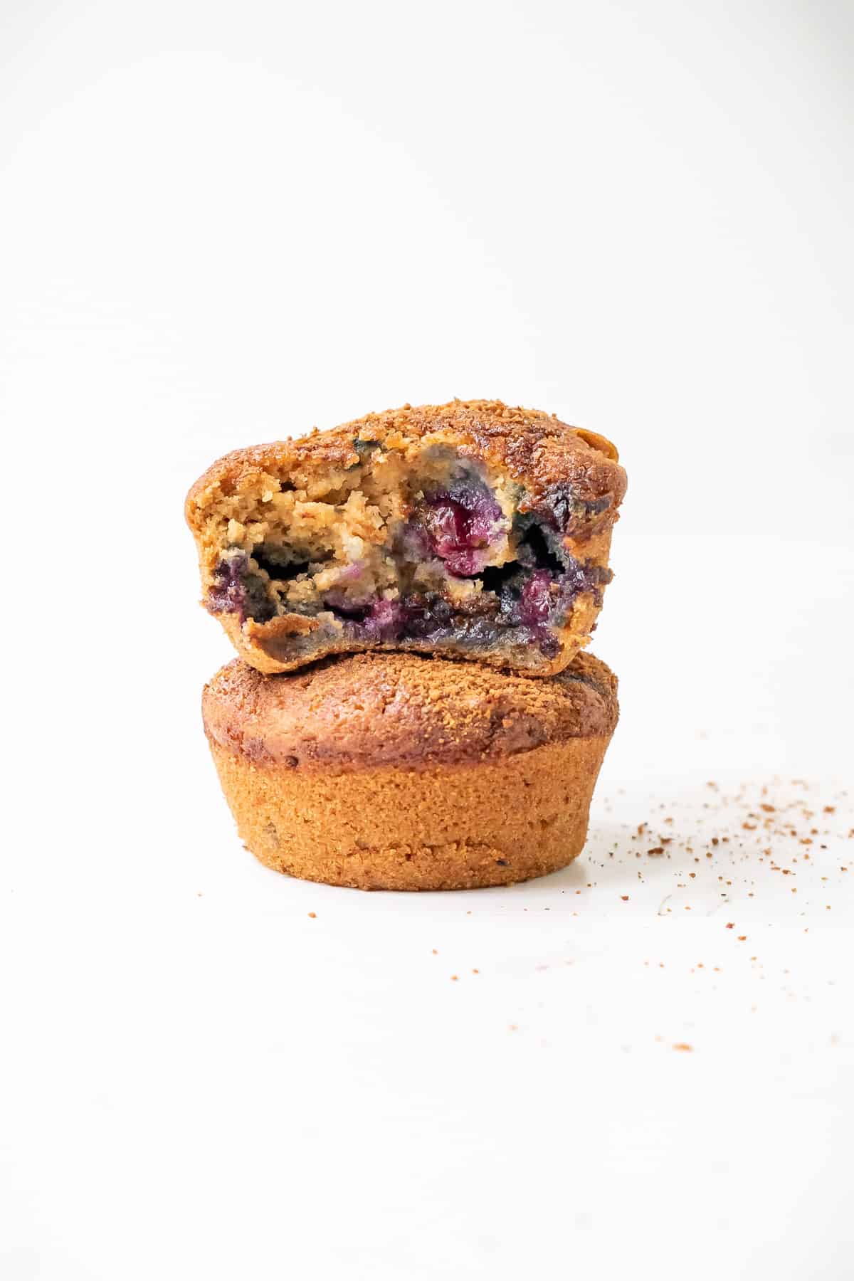 Two stacked gluten free blueberry muffins with a bite taken out of the top one to show a fluffy texture and tons of blueberries!