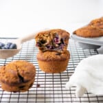 Two stacked gluten free blueberry muffins with a bite removed from one to show fluffy texture and tons of blueberries!