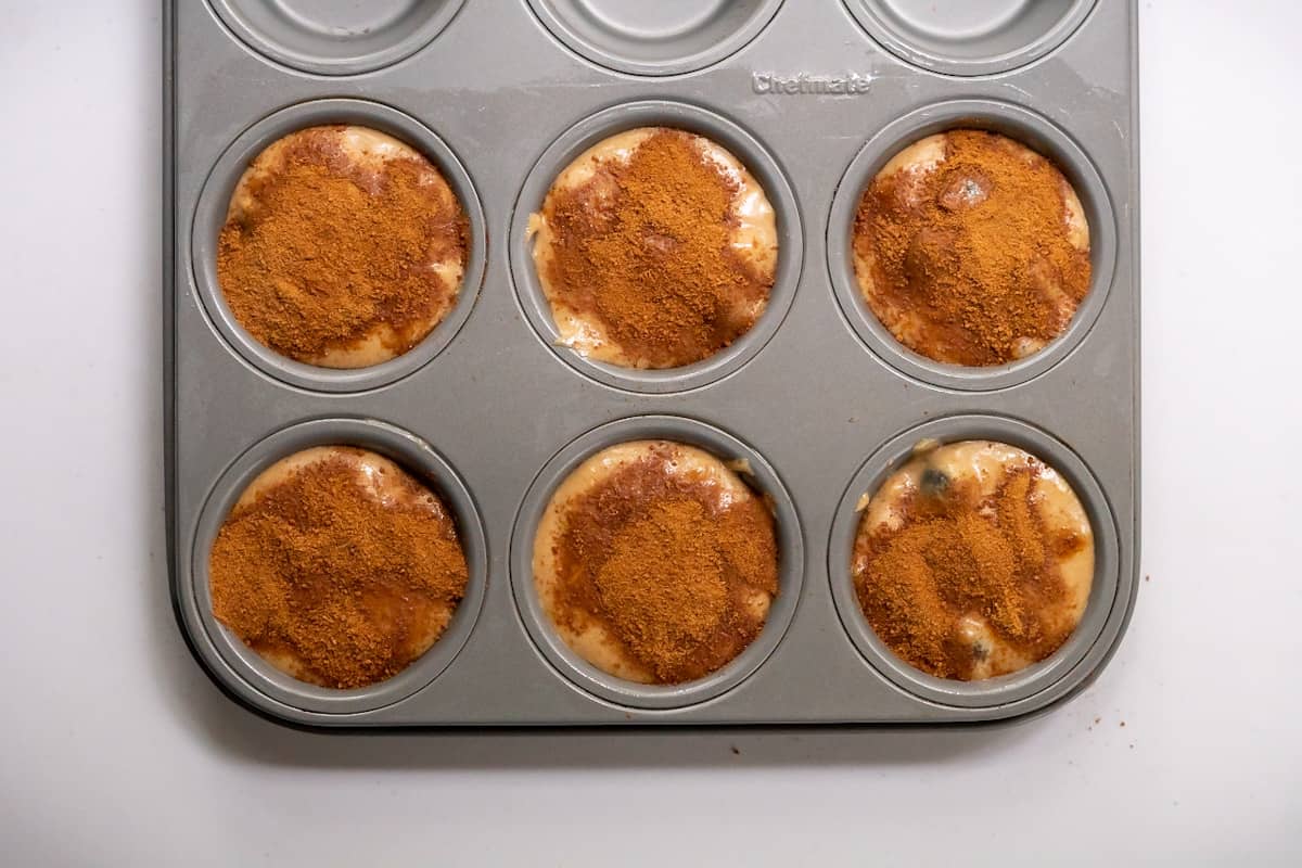 Cinnamon sugar sprinkled generously over six muffin cups filled with batter.