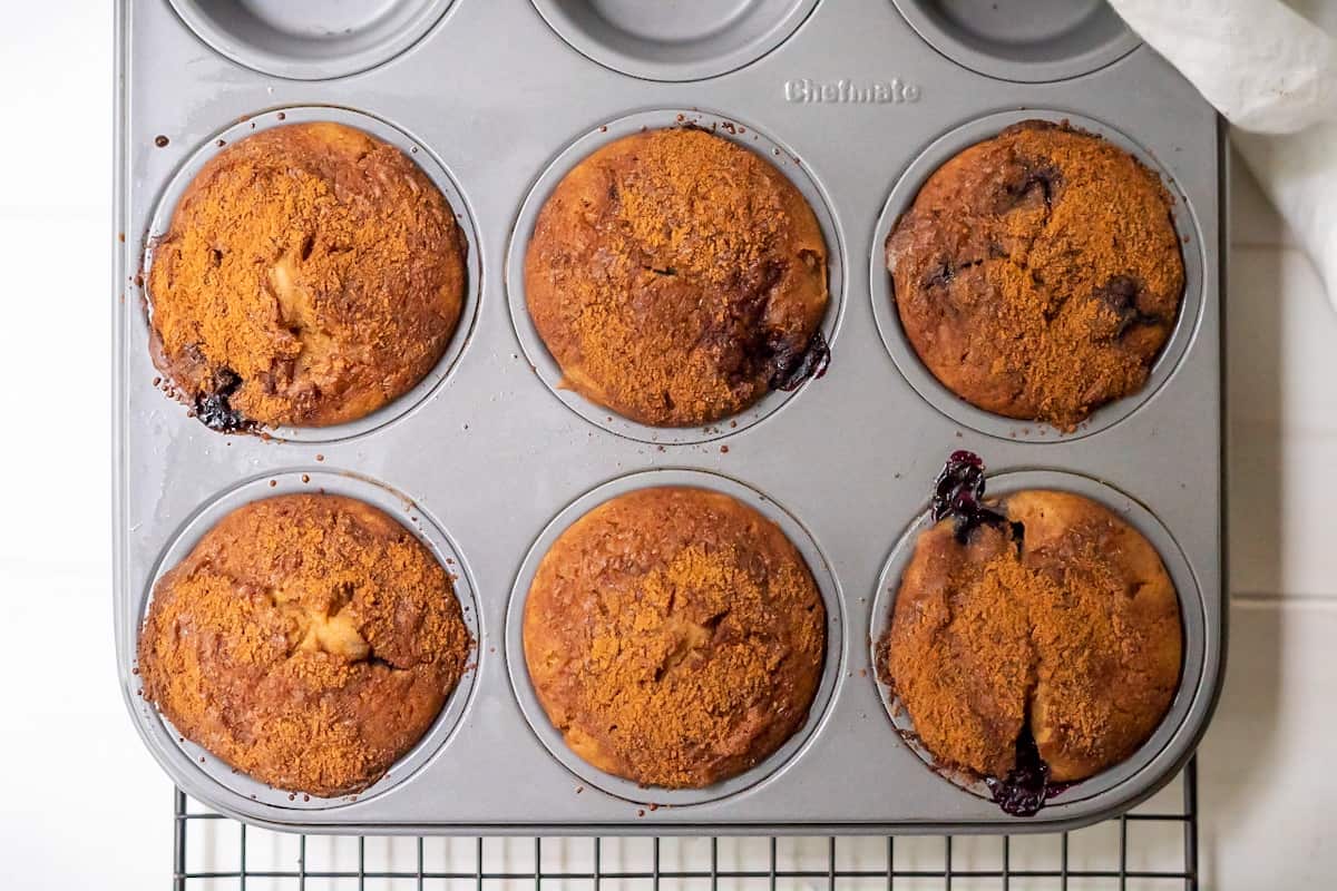 Six freshly baked gluten free blueberry muffins in a muffin tin and cooling.