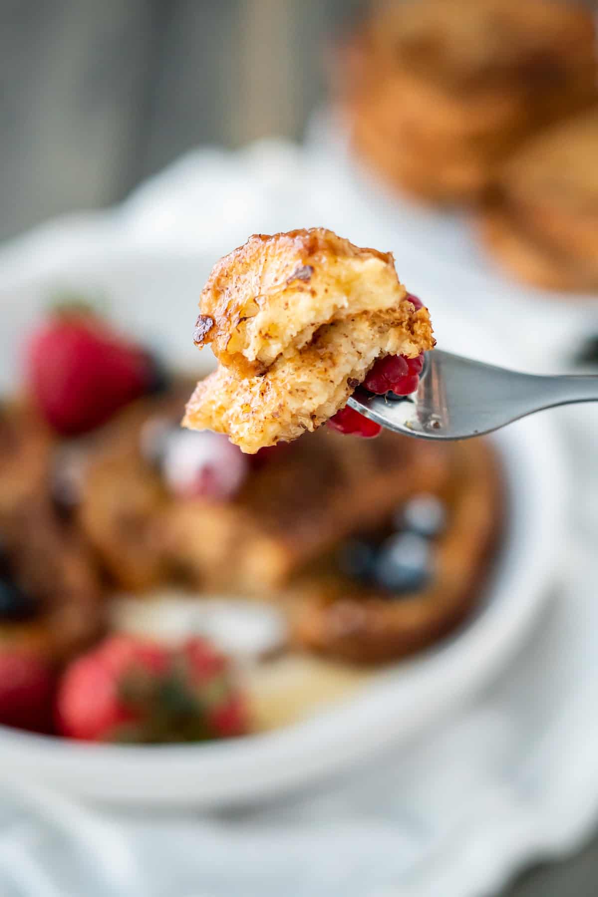 A bit of two slices of french toast with a fresh raspberry to show the fluffy souffle-like texture.