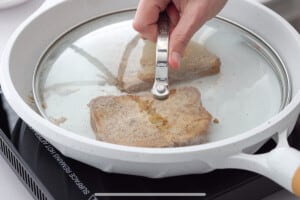 Frying two pieces of french toast in a frying pan with a lid over top.