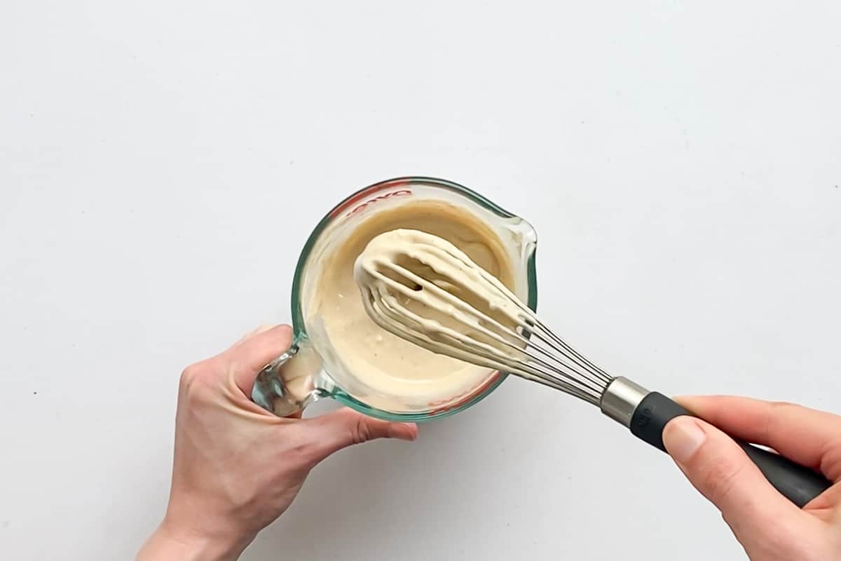 Overhead view of the whisk covered in vegan tahini pasta sauce to show it's super creamy texture.
