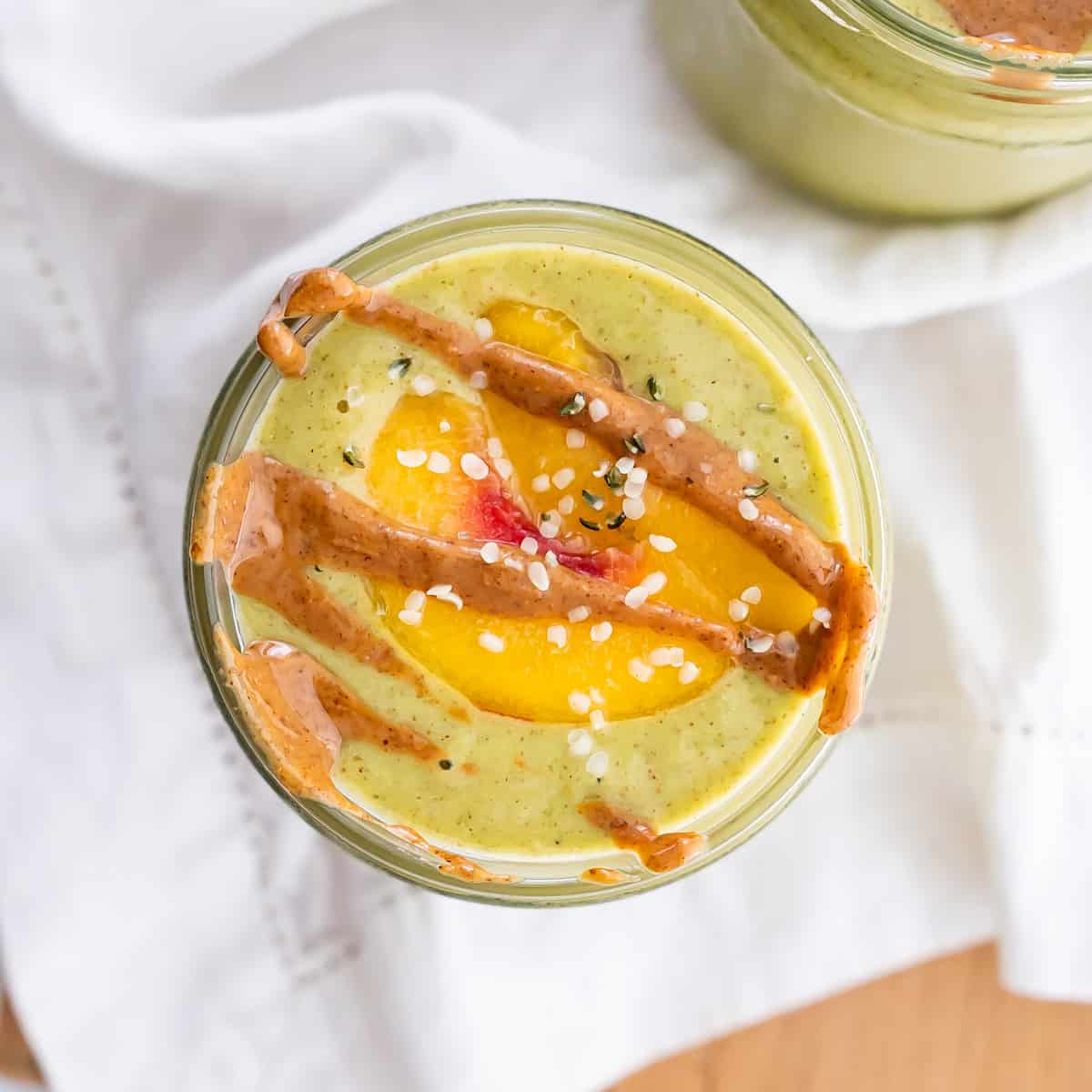 A green superfood breakfast smoothie topped with a peach slices and drizzle of almond butter.