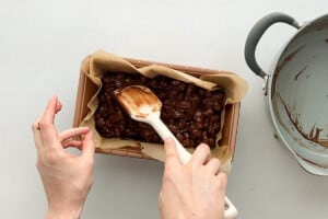 Using a rubber spatula to gently press the rocky road mixture into the corners of the pan.