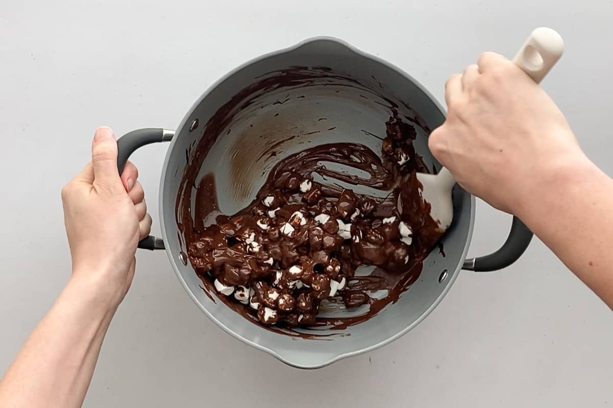 Using a silicon spatula to gently incorporate mini marshmallows into the chocolate and graham cracker mixture.