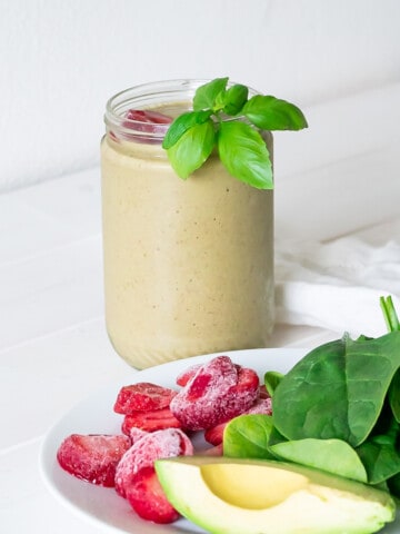 A tall glass of strawberry basil smoothie with a strawberry and basil leaves to garnish.