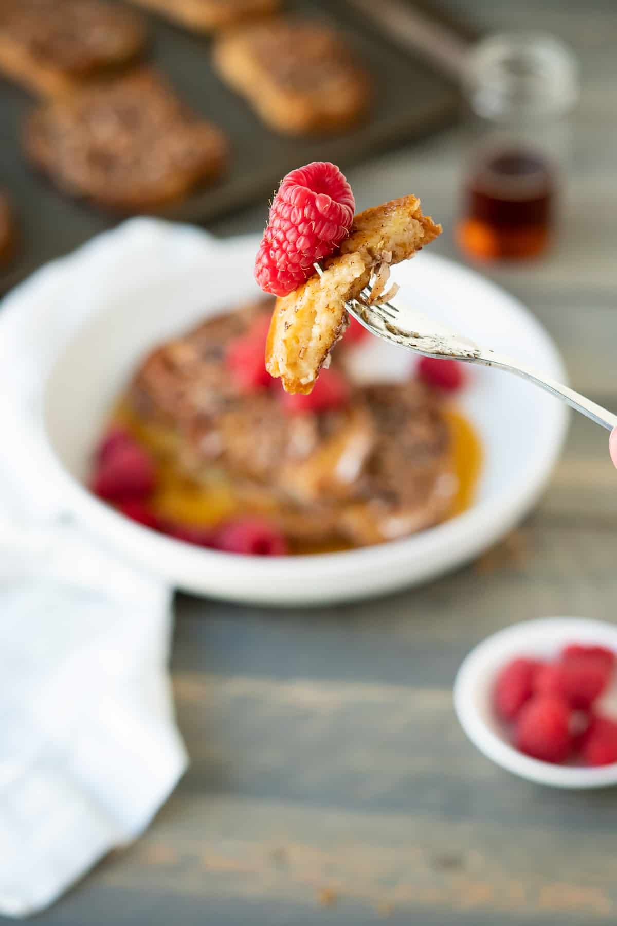 One bite of coconut crunch french toast on a fork with a fresh raspberry to show the crisp edges and soft inside!