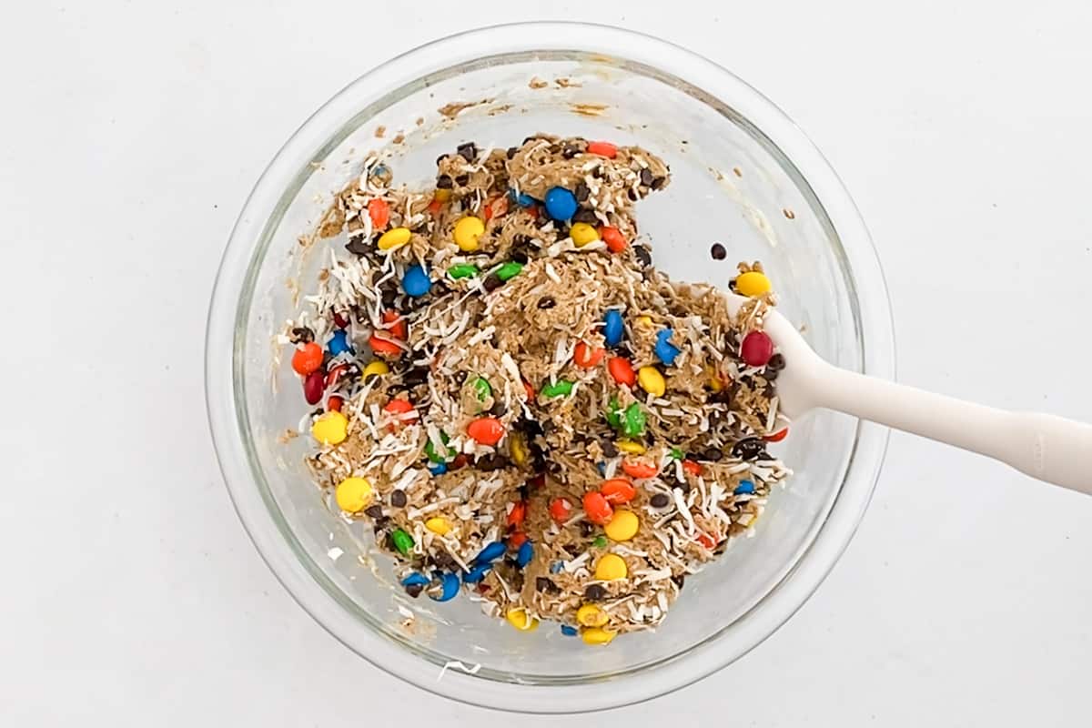 A mixture of fun ingredients in cookie dough including M&Ms, shredded coconut, and chocolate chips.