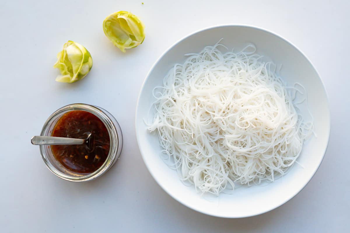 A dish of vermicelli rice noodles, fully cooked, and a jar of Vietnamese-inspired nuoc cham dressing.