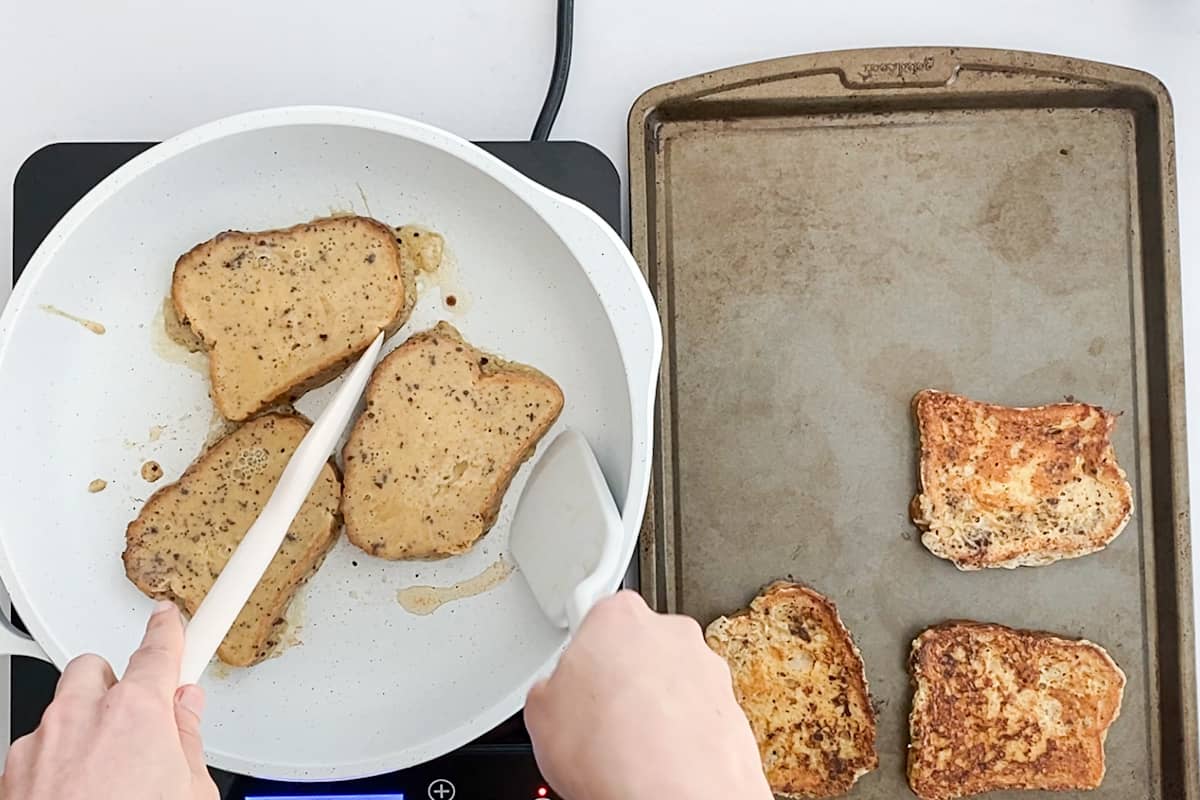 Flipping french toast from the skillet to a baking sheet.