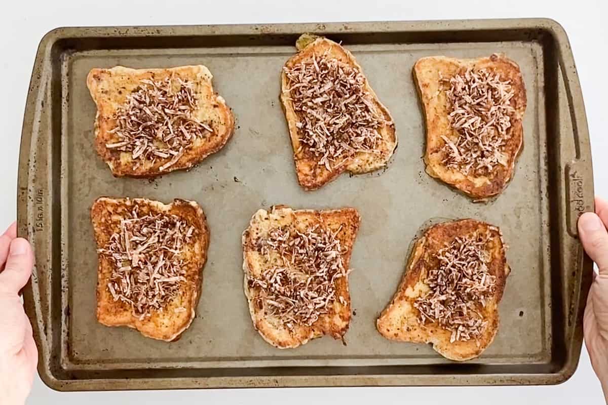 A baking sheet with six pieces of dairy-free french toast topped with coconut crunch topping.