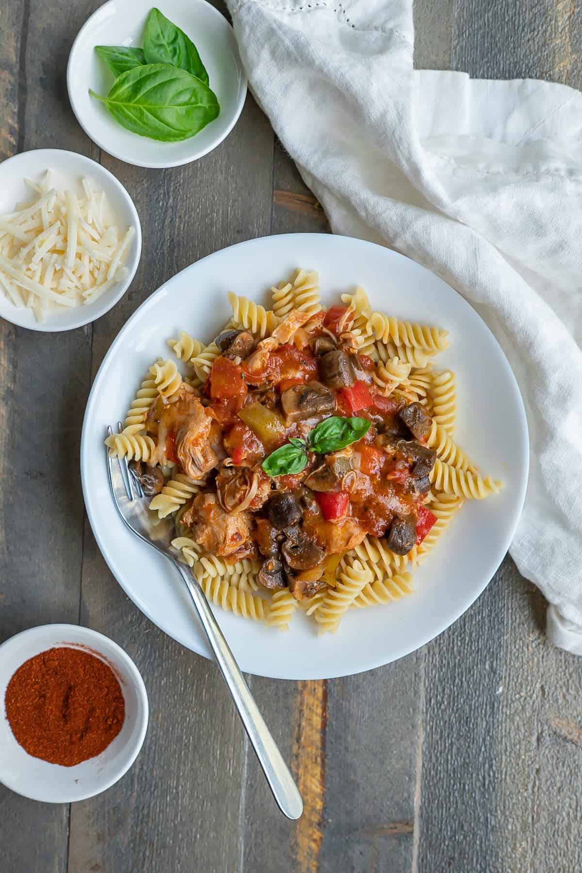 Instant Pot chicken cacciatore served over fusilli pasta on a plate with cheese and basil leaves on the side.