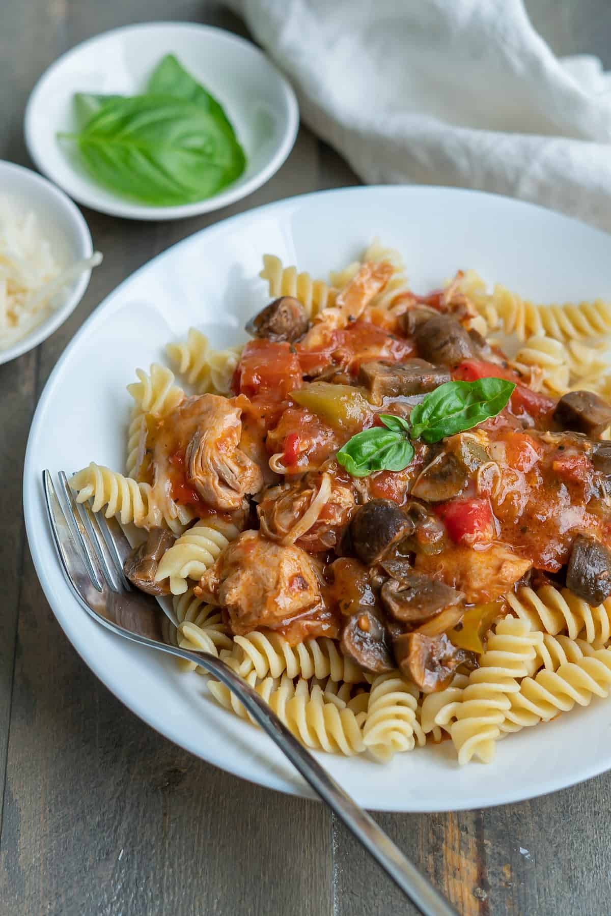 A bowl of instant pot chicken cacciatore served over pasta with fresh basil, chunky veggies, and tender chicken.