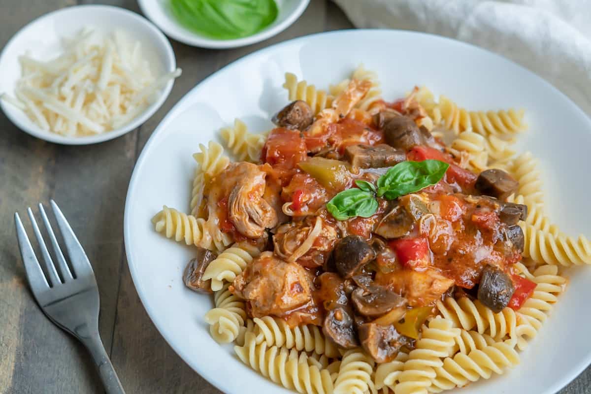 Easy Chicken Cacciatore served over fusilli pasta with basil to garnish and freshly grated cheese on the side.