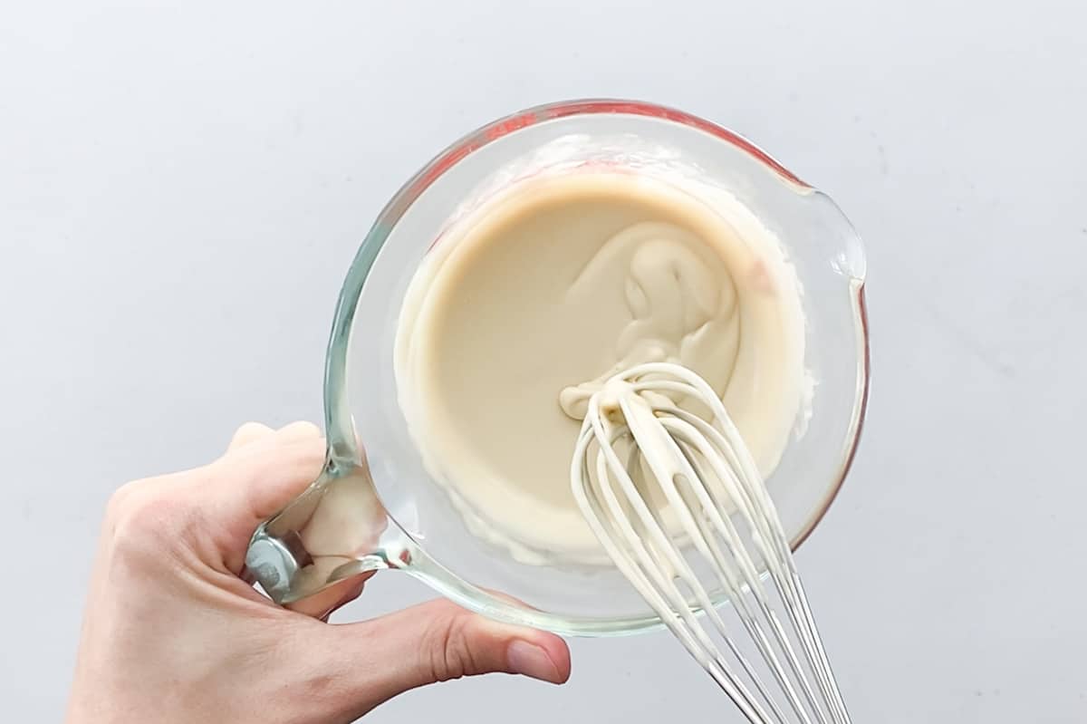 A creamy mixture of egg, vanilla extract, and coconut milk in a glass measuring cup with a whisk.