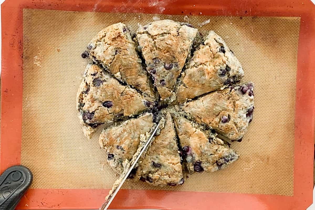 A knife nudging apart the blueberry scone wedges while they are partially baked on a silicone mat lining a baking sheet.