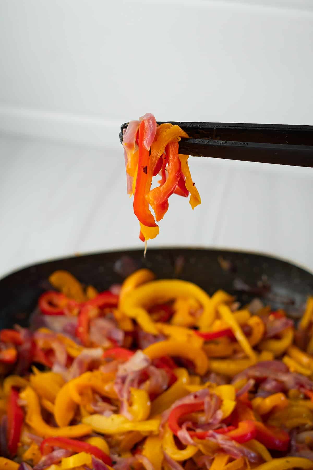 Tongs holding up several sauteed onions and peppers to show the soft, caramelized texture.