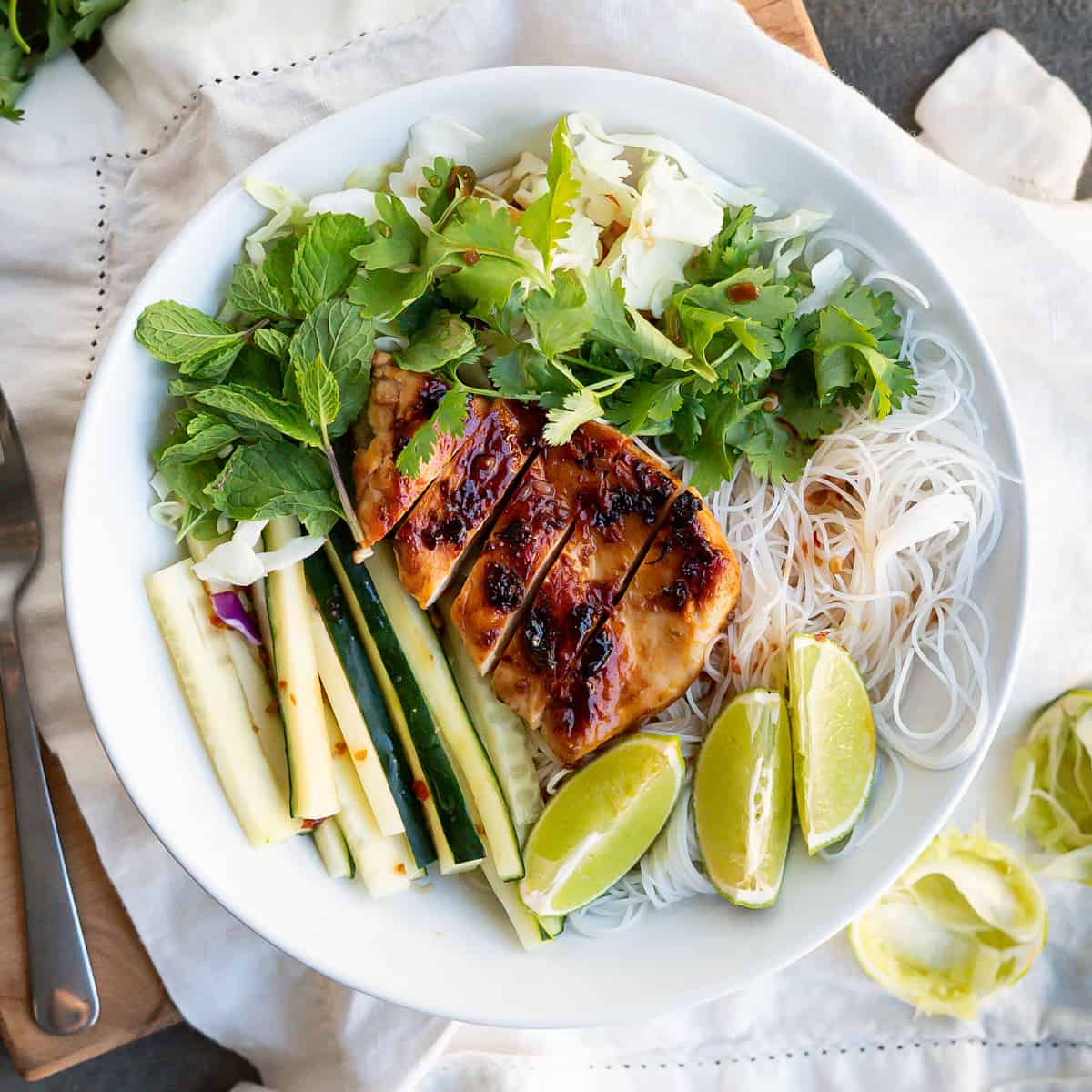 Overhead view of an assembled bowl of Vietnamese Noodle Salad with Nuoc cham dressing and limes wedges to garnish.