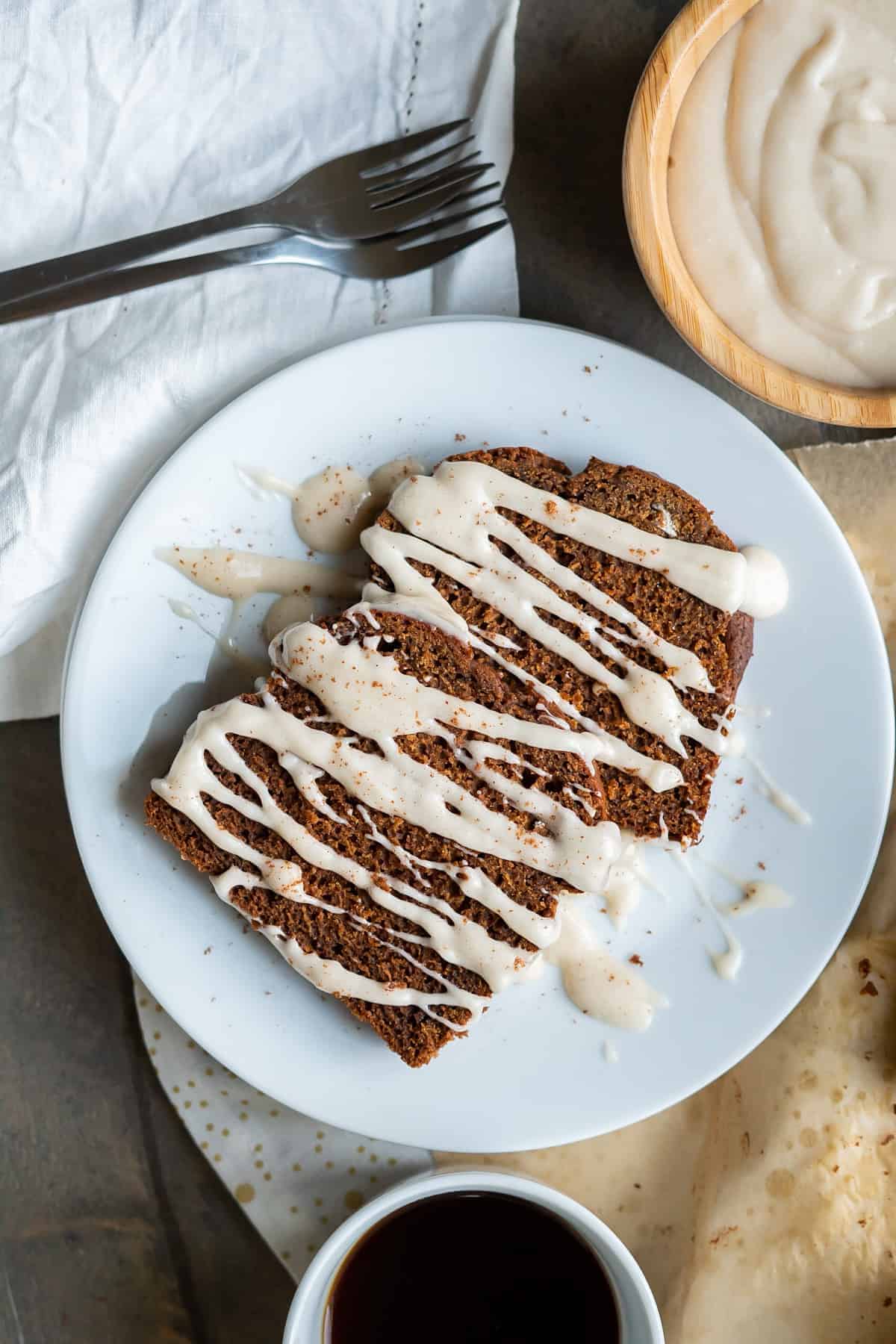 Two slices of easy gingerbread cake drizzled with icing and served with a cup of coffee and extra icing on the side.
