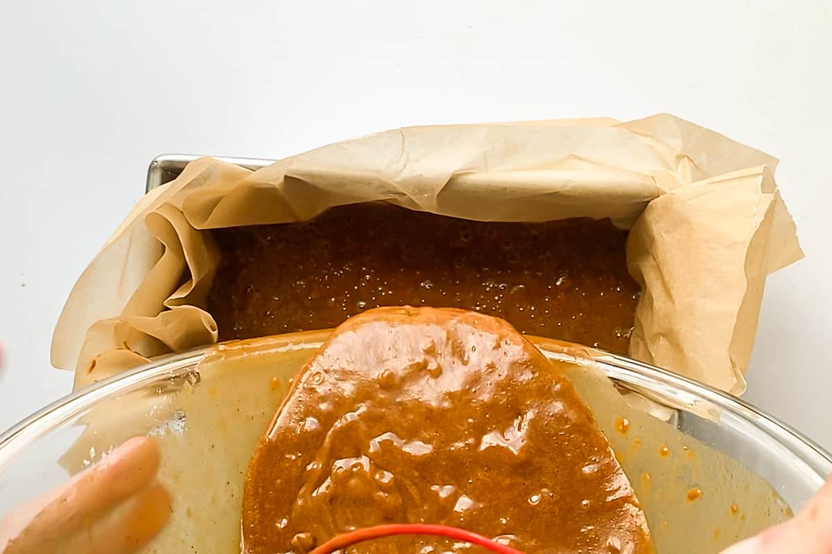 Pouring the bowl of gingerbread cake batter into a loaf pan.