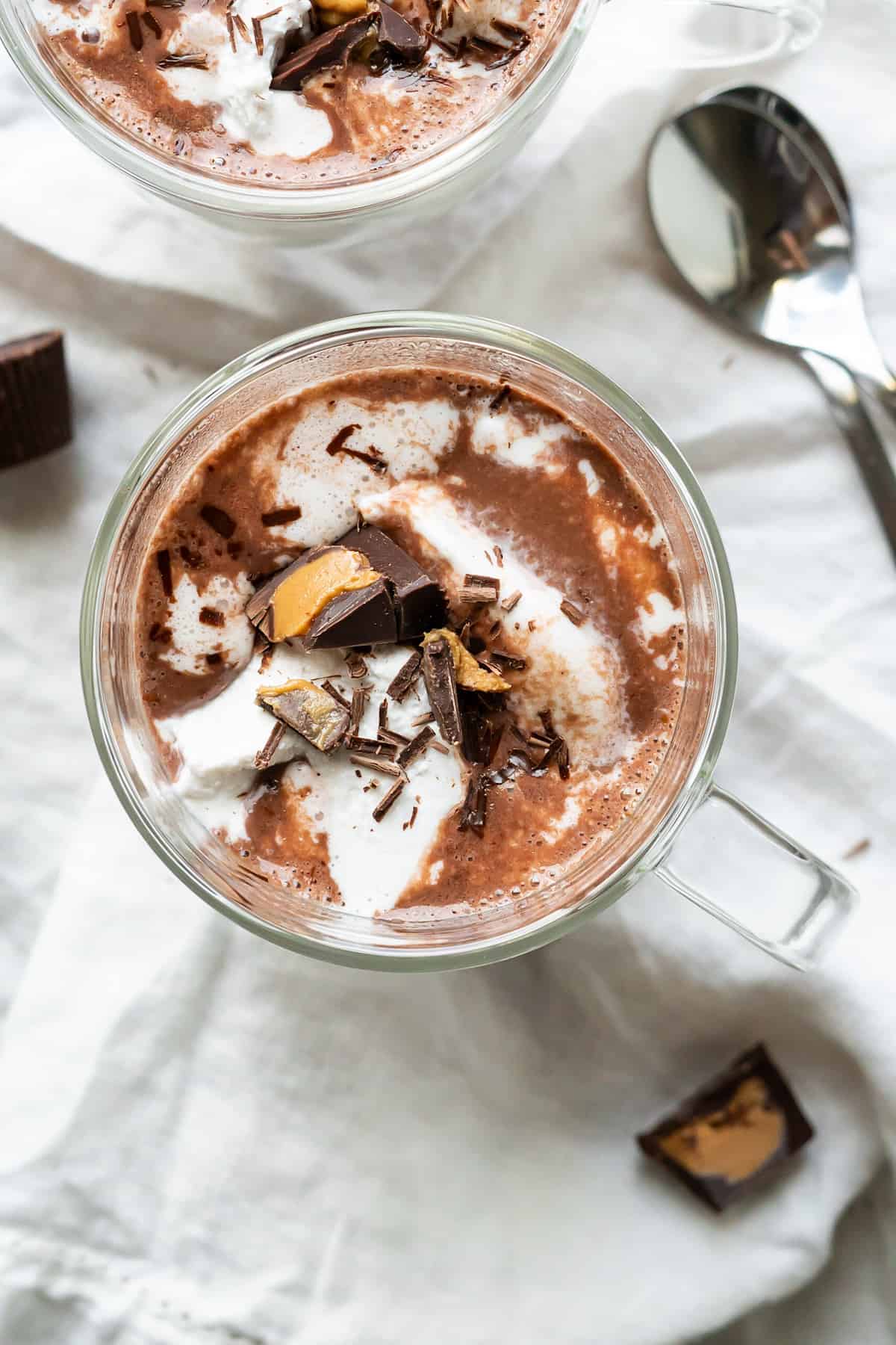 Overhead view of a mug of peanut butter hot chocolate topped with whipped cream, chocolate shavings, and a chopped peanut butter cup.