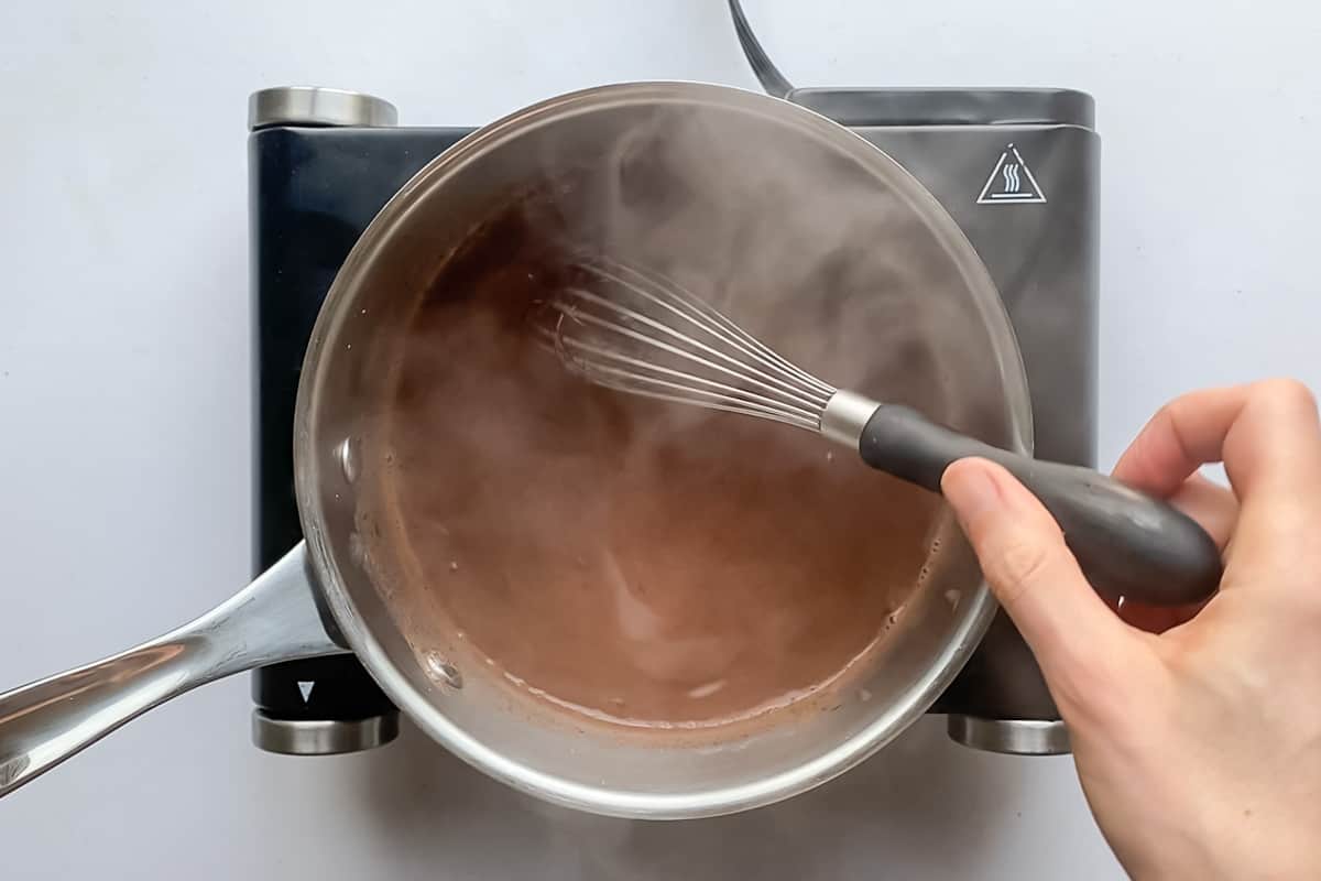 Whisking hot chocolate in a small pan on an electric burner.