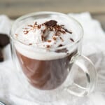 A side view of a cup of Italian hot chocolate topped with whipped cream, chocolate shavings and a piece of chocolate.