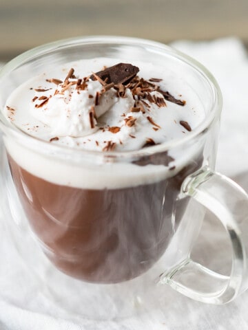 A side view of a cup of Italian hot chocolate topped with whipped cream, chocolate shavings and a piece of chocolate.