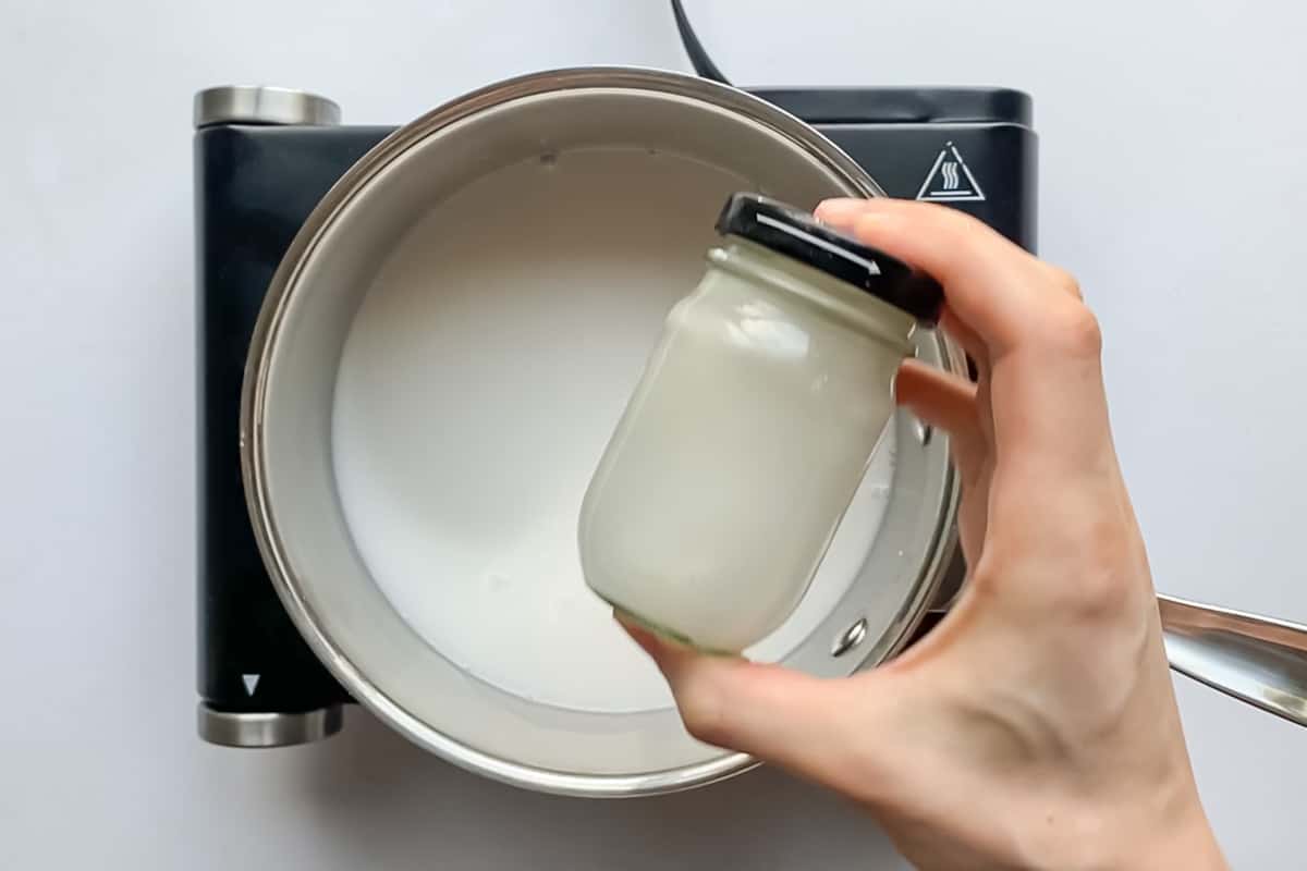 A small pot of milk warms on a burner while a starch mixture is shaken in a jar.