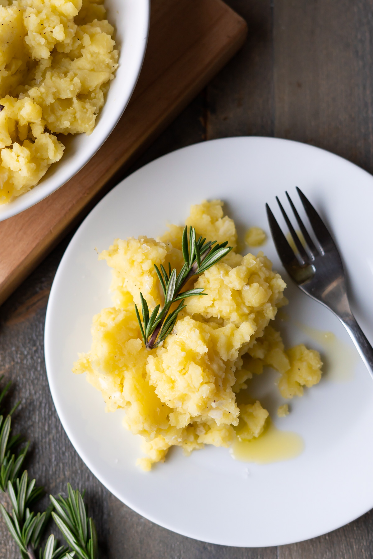A serving of olive oil mashed potatoes on a plate, garnished with fresh rosemary.