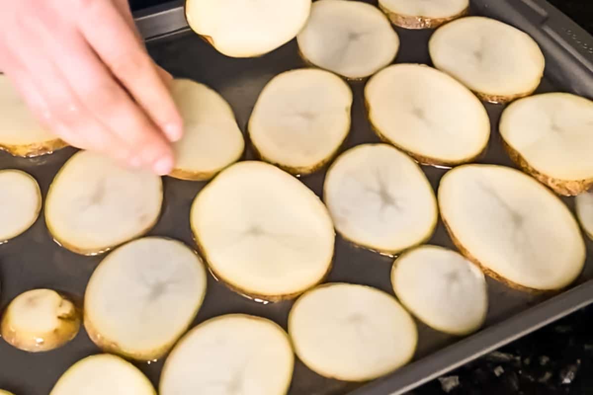 Potato slices in a single layer on a baking sheet covered in oil.