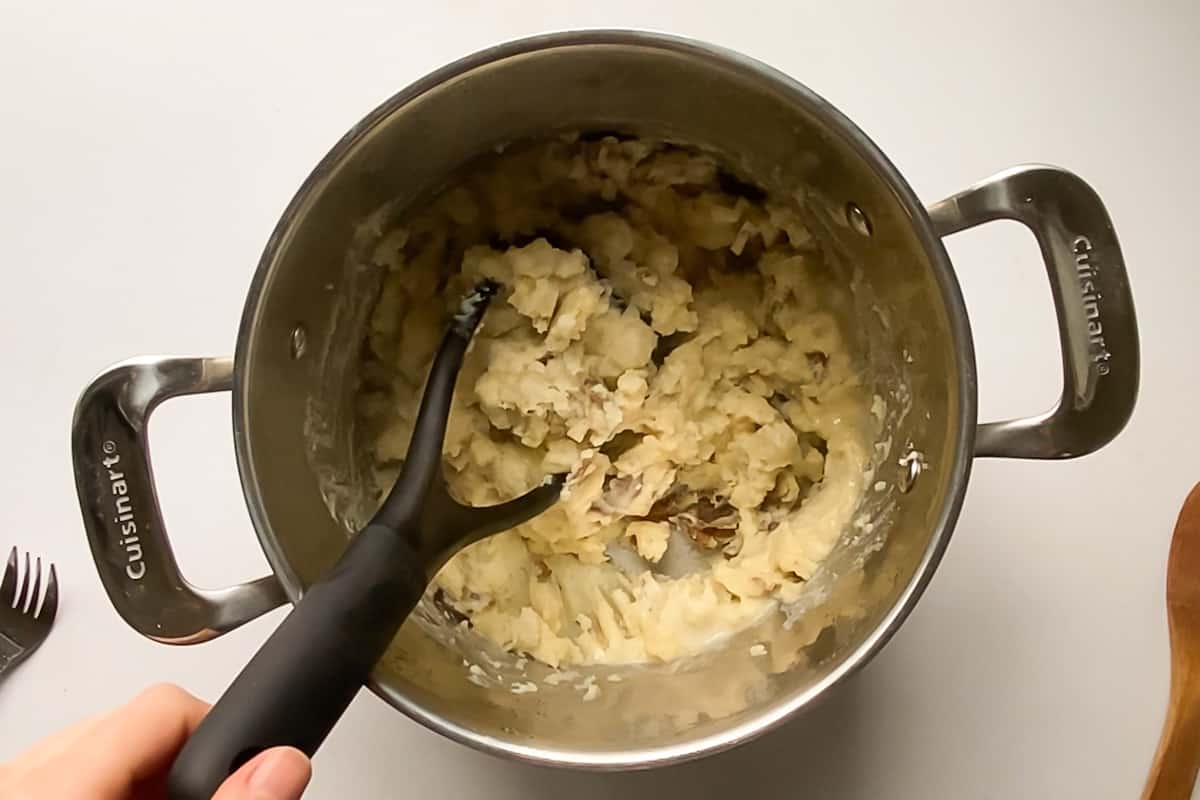 A large pot of mashed potatoes with a potato masher.