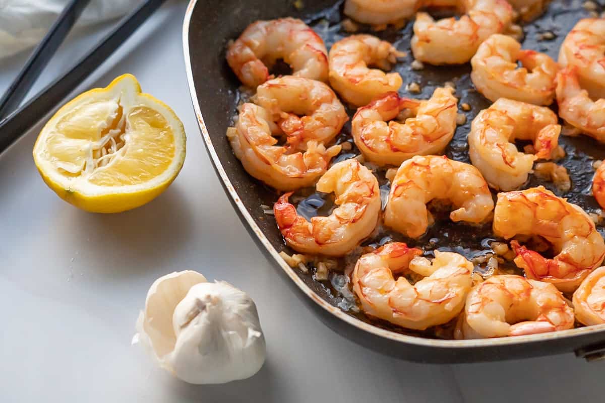 Finished shrimp scampi in a large skillet with lemon and garlic on the side.