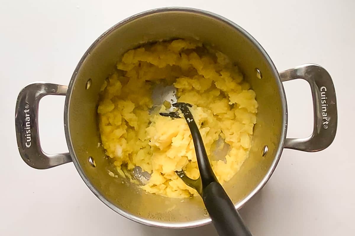 Using a potato masher to cream olive oil mashed potatoes without milk or butter.