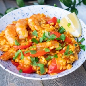 An easy shrimp paella served in a bowl with a lemon wedge and garnished with parsley.
