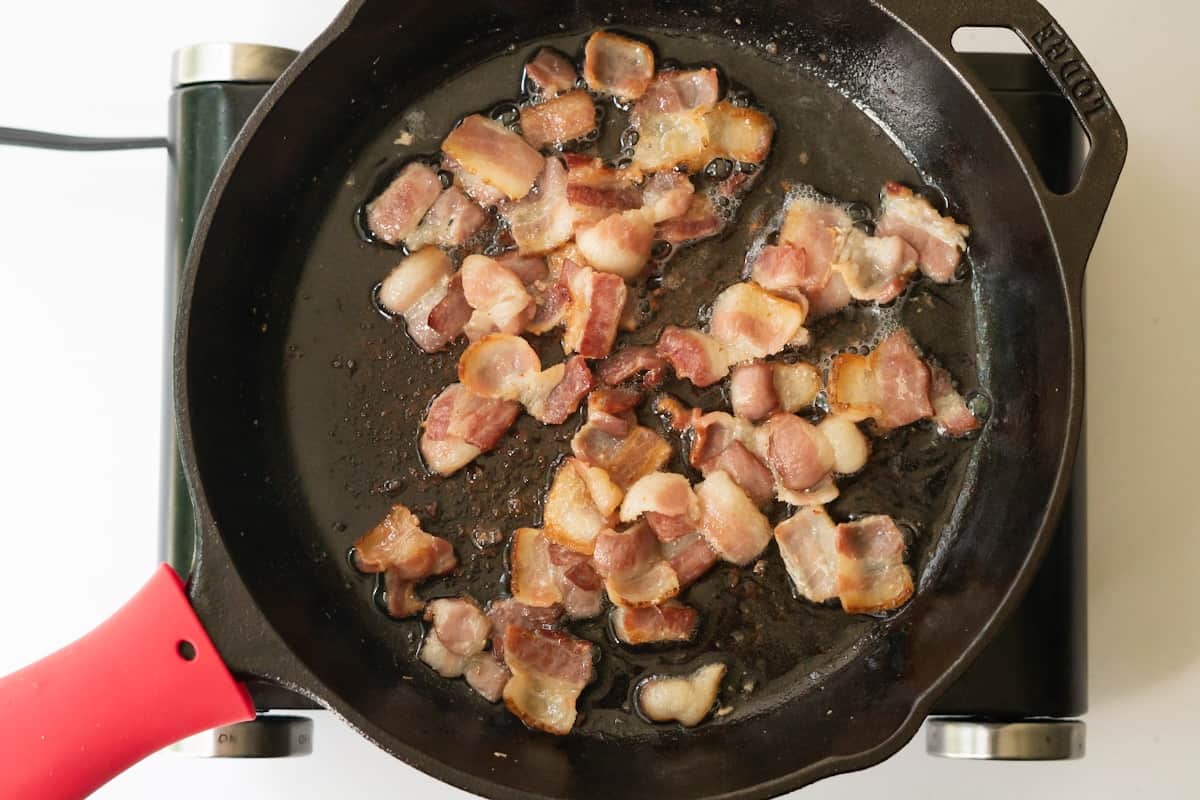 Crispy bacon pieces frying in a cast iron skillet.