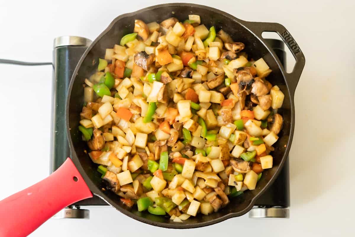 A cast iron skillet filled with potatoes, vegetables, and spices.