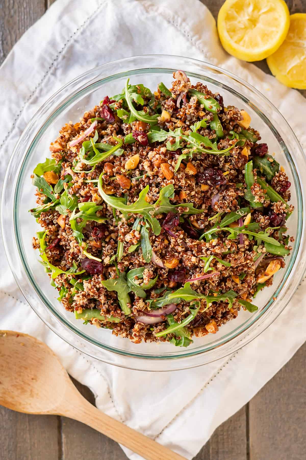 A large glass serving bowl of arugula quinoa salad with almonds and green beans.