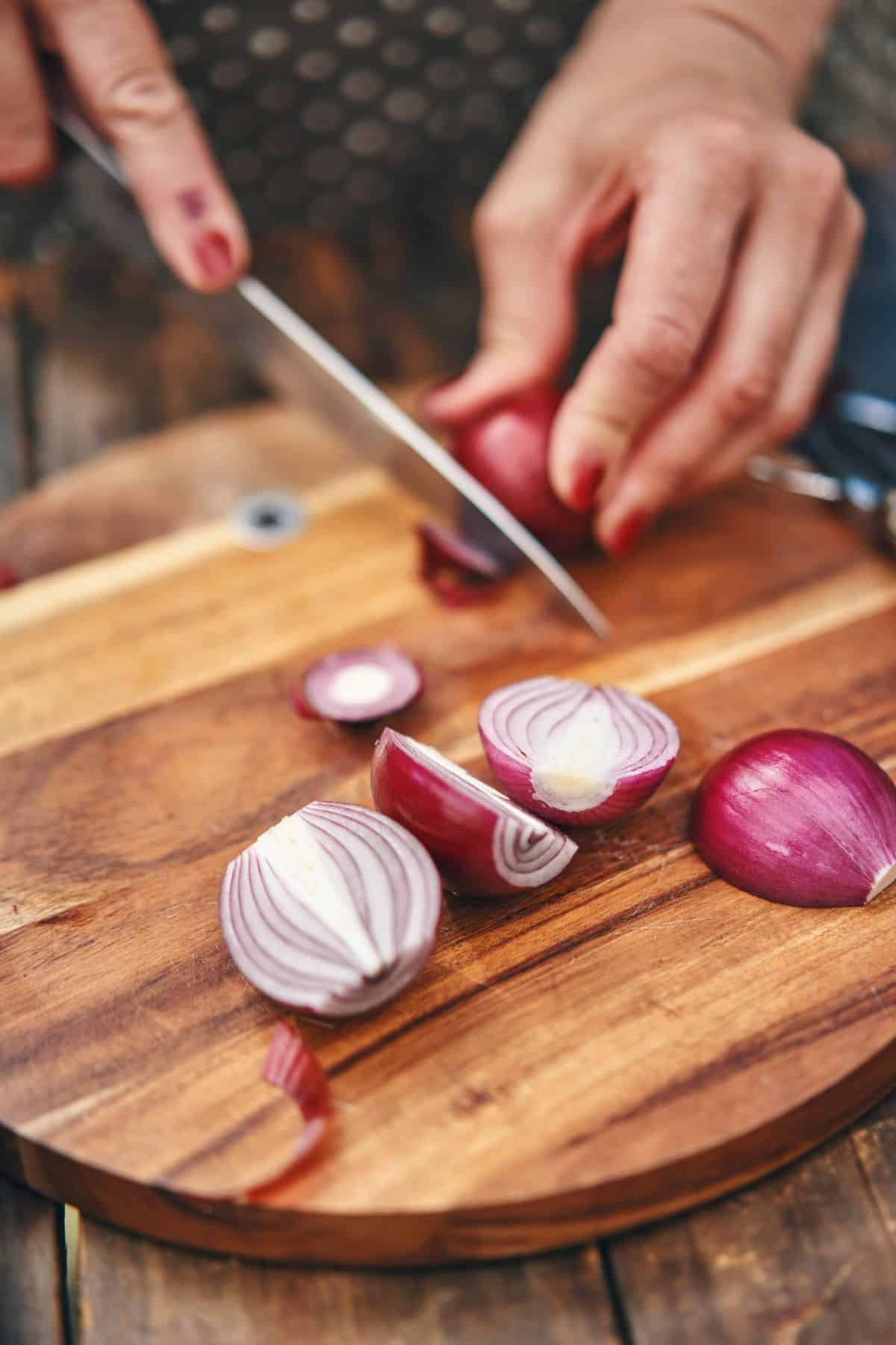 Chopping onions on a wooden cutting board with a knife.
